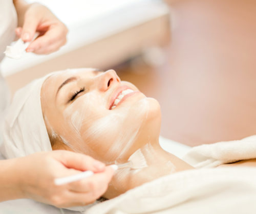 Cosmetology. The hands of a cosmetologist apply a cleansing mask for the face. Smiling girl on facial cleansing procedure