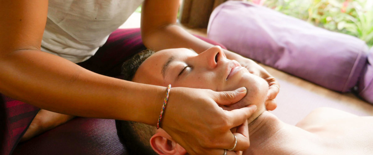 natural lifestyle portrait of young beautiful and exotic Asian Thai therapist woman giving traditional head and facial Balinese massage to Caucasian man at alternative medicine healing spa